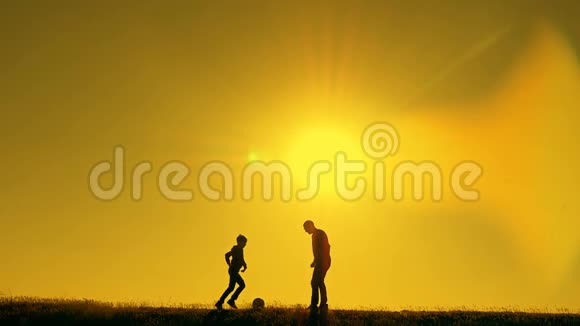 日落时分父亲和儿子在公园里踢足球在灿烂的阳光下剪影视频的预览图
