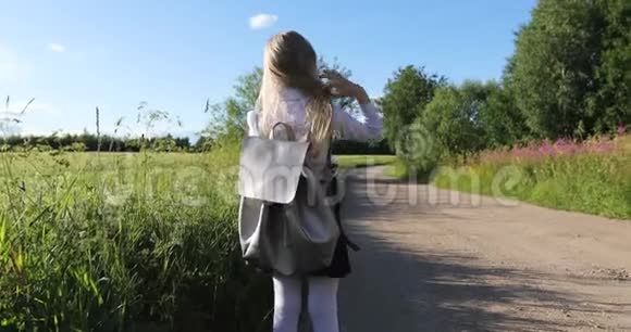 穿着白色衬衫和黑色裙子的学校女孩正在沙路旁穿过田野和森林视频的预览图