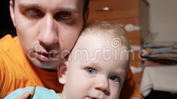 一个2岁有魅力的男孩和一个做自拍的父亲微笑着看着家里的相机视频的预览图
