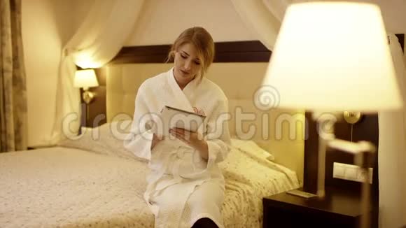 年轻漂亮的女人坐在床上在平板电脑上摆弄着东西视频的预览图