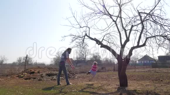父亲一边在公园里玩一边把女儿推到秋千上视频的预览图