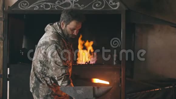 长胡子的青年铁匠在铁匠的铁砧上用火花烟火手工锻造铁水视频的预览图