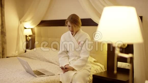 年轻女子坐在笔记本电脑旁边的床上打着电话视频的预览图