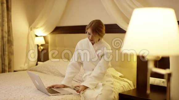 年轻女子坐在笔记本电脑前的床上打着电话视频的预览图