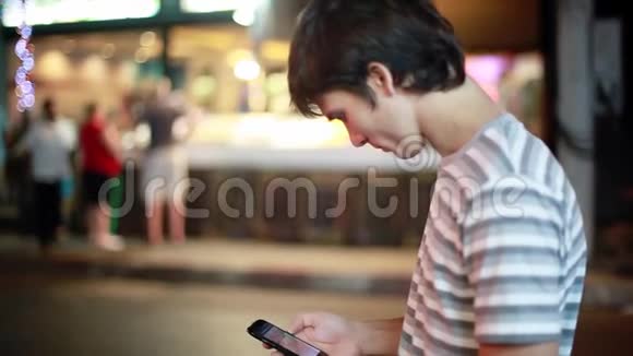帅哥在街上使用他的智能手机街道上的城市灯光模糊现代技术1920x1080视频的预览图