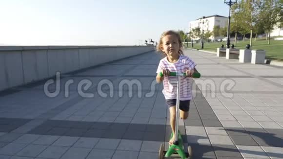 阳光明媚的夏日快乐可爱的小女孩在公园里骑着踢踏板车视频的预览图