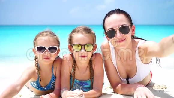 妈妈和小女孩在沙滩上躺在白沙上自拍幸福的一家人带着自画像度假放松视频的预览图