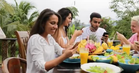 使用智能手机的人说吃健康的素食朋友在热带露台上交流视频的预览图