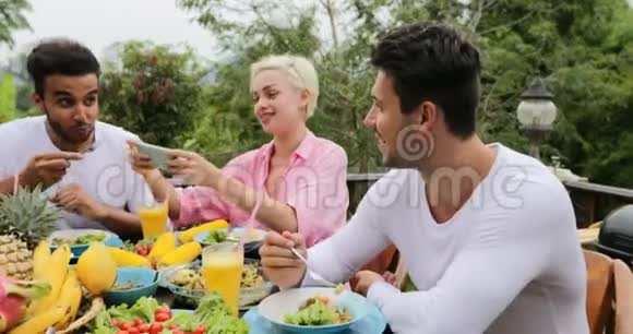 使用智能手机的人说吃健康的素食朋友在热带露台上交流视频的预览图