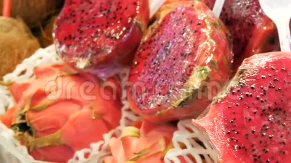 西班牙水果市场柜台上的椰子旁边的成熟多汁的红粉色火龙果视频的预览图
