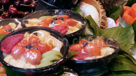 将不同的草莓水果芒果猕猴桃等混合在水果市场柜台上的塑料盘子里视频的预览图