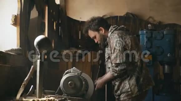 在传统的铁匠铺上手工打磨金属刀的大胡子青年铁匠视频的预览图