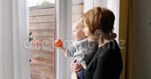 祖母带着孙子在家透过窗户看着视频的预览图