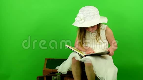 女孩坐在手提箱上读这本书小女孩在色度键背景旅行概念视频的预览图