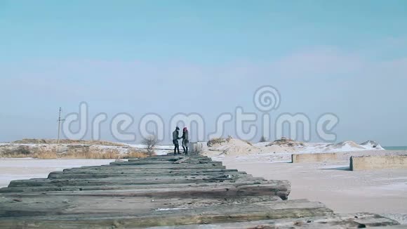 小伙子和姑娘在冬天穿着走在木板桥上一个美丽的冬天阳光明媚的日子视频的预览图
