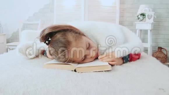 小女孩穿着睡衣一边看书一边睡着了上面铺着白色的毛毯视频的预览图
