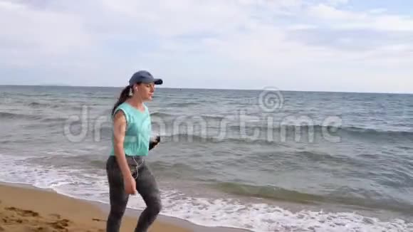 带着耳机的运动女性沿着海滩散步视频的预览图