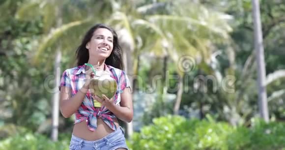 美丽的女孩喝椰子鸡尾酒棕榈树上快乐的微笑青年妇女旅游视频的预览图