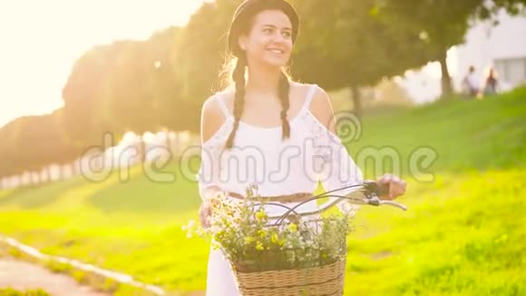 夕阳下年轻漂亮的女人站在她的自行车附近慢动作视频的预览图