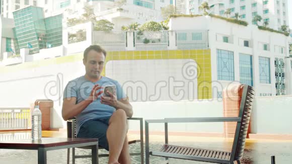 在游泳池附近的露台上等女朋友的人用智能手机城市景观视频的预览图