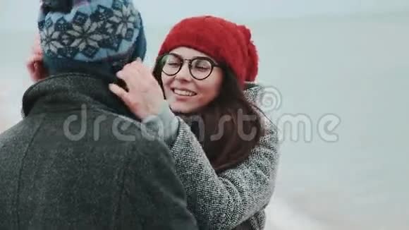 在海边的一对夫妇穿着冬衣戴着红色帽子和眼镜的女孩视频的预览图