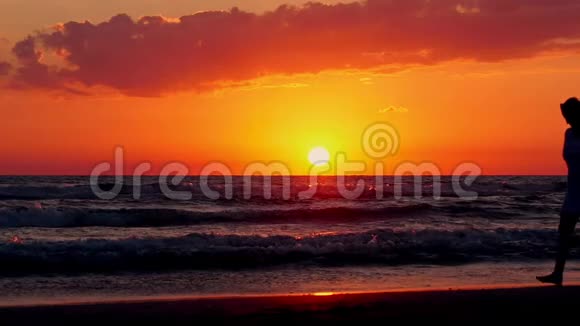 夕阳背景下一位年轻女子在海边漫步的剪影视频的预览图