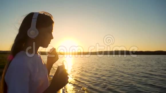 女孩青少年耳机和手机在日落慢动作视频的预览图