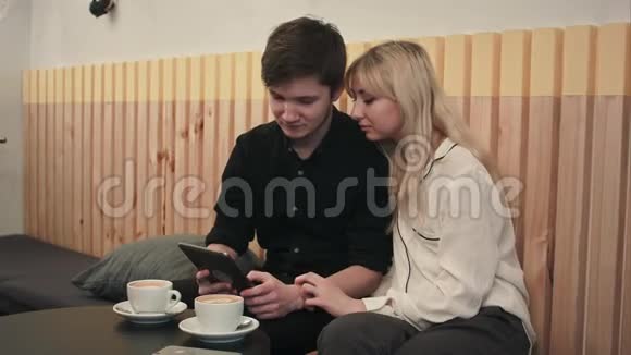 一对年轻夫妇在咖啡馆里喝咖啡用数码平板电脑视频的预览图