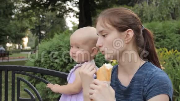 一个年轻女孩坐在长凳上旁边站着一个穿着着一个穿着淡紫色连衣裙的小女孩旁边有一个白色的圆点图案视频的预览图