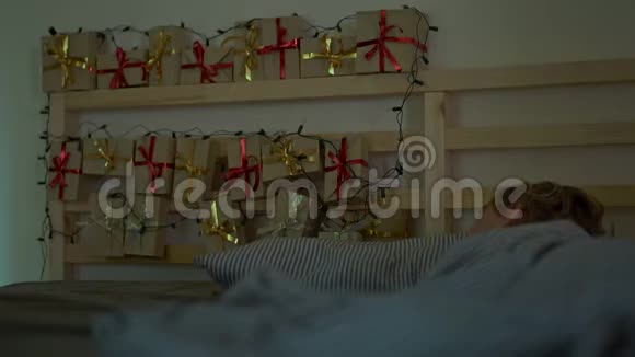 一个小男孩睡在他的床上他的床背上有一盏圣诞灯照着他的圣诞日历视频的预览图