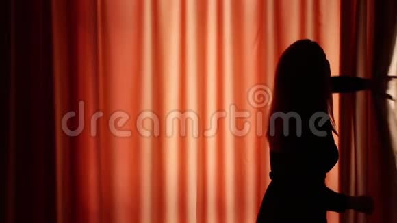 年轻女子在一间黑暗的房间里拉开窗帘看窗外冬天的景色视频的预览图