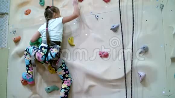 孩子爬上专门的登山墙7岁的女孩在安全设备上从事岩石工作视频的预览图