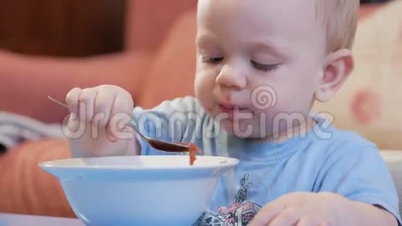 一个2岁有魅力的男孩自己在吃红汤勺子和手流动的液体健康饮食的概念视频的预览图