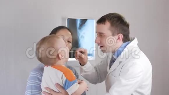一位年轻的男性儿科医生检查婴儿的喉咙这个男孩在他母亲怀里视频的预览图