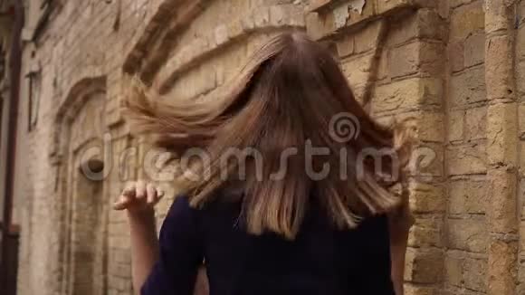穿着蓝色裙子的女孩在镜头前对着砖墙背景摆姿势视频的预览图