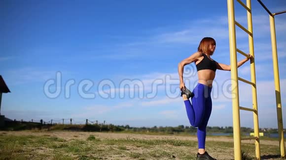 穿着蓝色裤腿的女孩把脚揉在一个垂直的梯子上伸展肌肉准备训练视频的预览图