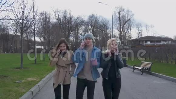 年轻人一个男人和两个女孩在公园里散步打电话晴天好视频的预览图