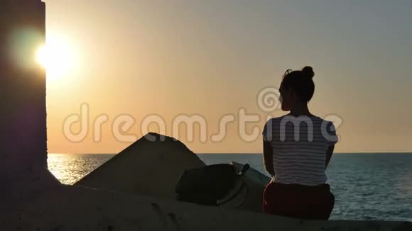 年轻女子坐在岩石上看着夕阳的大海视频的预览图