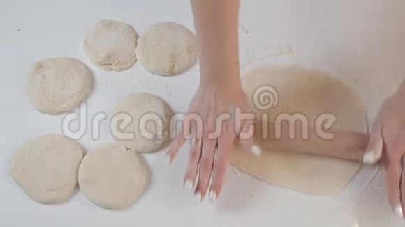 女面包师用擀面杖在木桌和面粉上的配料背景上滚动面团视频的预览图