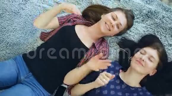 两位戴耳机听音乐跳舞躺在床上微笑的漂亮女孩的俯视图视频的预览图