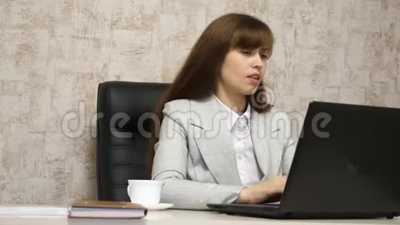 漂亮的女孩坐在办公室的椅子上用笔记本电脑打字年轻的女商人在电脑上工作女孩视频的预览图