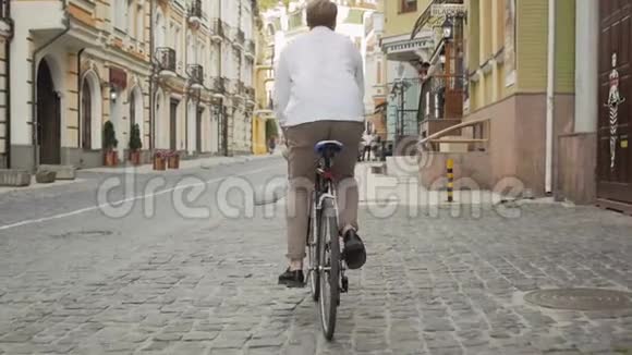 在铺好的道路上骑着老式自行车的时尚时髦男子的划片镜头视频的预览图