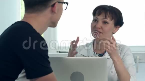 友好的女医生咨询坐在办公桌旁的男性病人咨询笔记本电脑视频的预览图