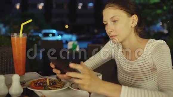 快乐的女人使用智能手机和短信晚上坐在餐厅视频的预览图