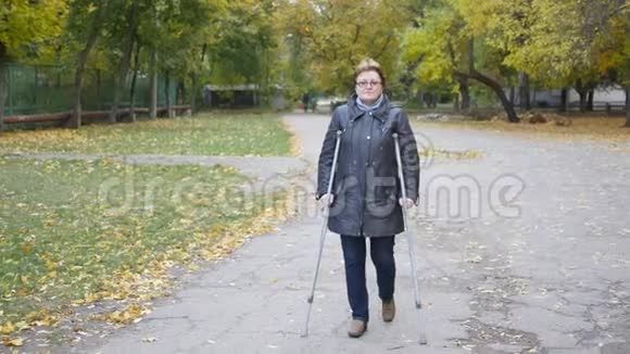 一位脚受伤的妇女拄着拐杖走在公园里视频的预览图