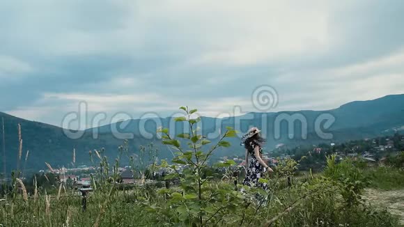 年轻的黑发女人戴着帽子和连衣裙在夏天的户外散步蓝天上有云和山视频的预览图