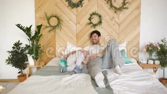 快乐英俊的年轻父亲躺在床上和儿子玩耍视频的预览图
