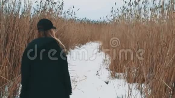 年轻的金发女孩走在雪道上在干燥的草地上在冬天阴天视频的预览图