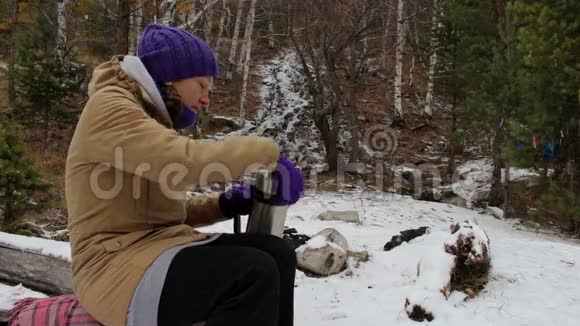 在冬天的森林里年轻的女人从一个热水瓶里倒茶视频的预览图