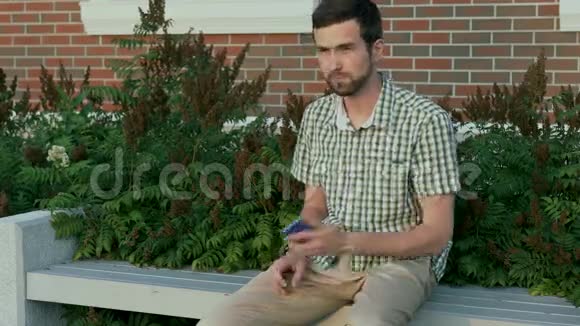 穿着休闲服的男人坐在长凳上用智能手机给他的朋友打电话视频的预览图